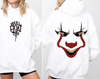 May include: White hoodie with a front graphic that says "You'll Float Too" in black. The back of the hoodie features a graphic of a clown face with red accents and black details. The hoodie has a hood and long sleeves.