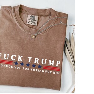 a brown t-shirt with a political statement printed on it, along with a necklace and some decorative elements.