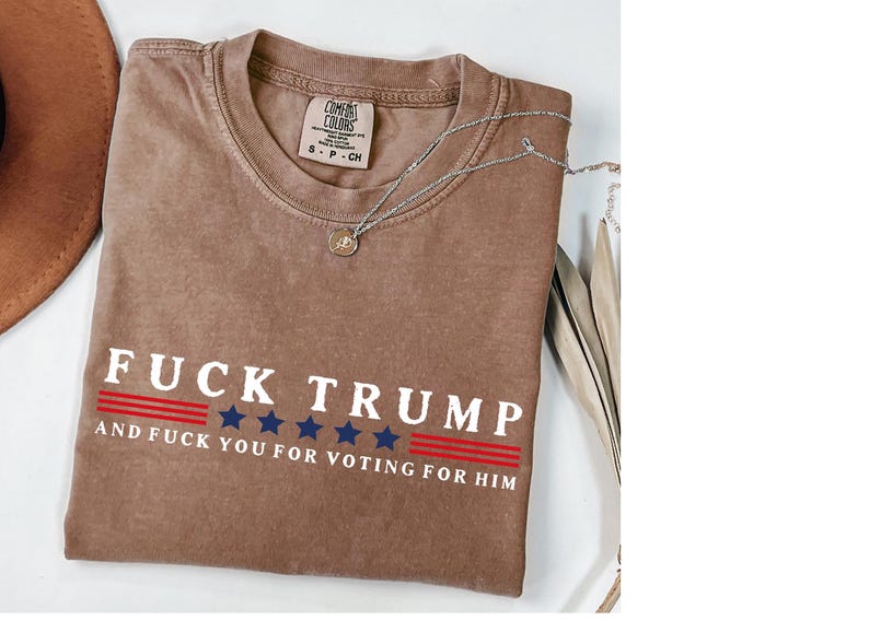 a brown t-shirt with a political statement printed on it, along with a necklace and some decorative elements.