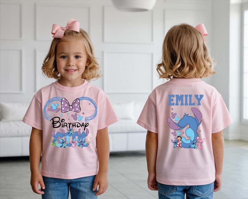 A young girl wearing a pink t-shirt with a cartoon character and the text "Birthday" printed on it, standing in a room with a white wall and a couch.