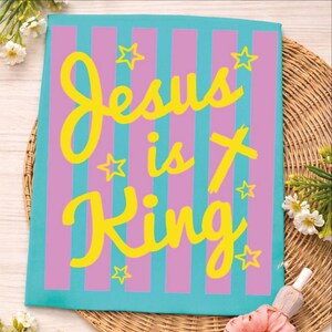 A colorful poster with the text "Jesus is King" in yellow and pink letters, surrounded by pink and purple stripes and stars.