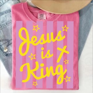 A pink t-shirt with yellow text and stars printed on it, along with a beige hat and some denim jeans.