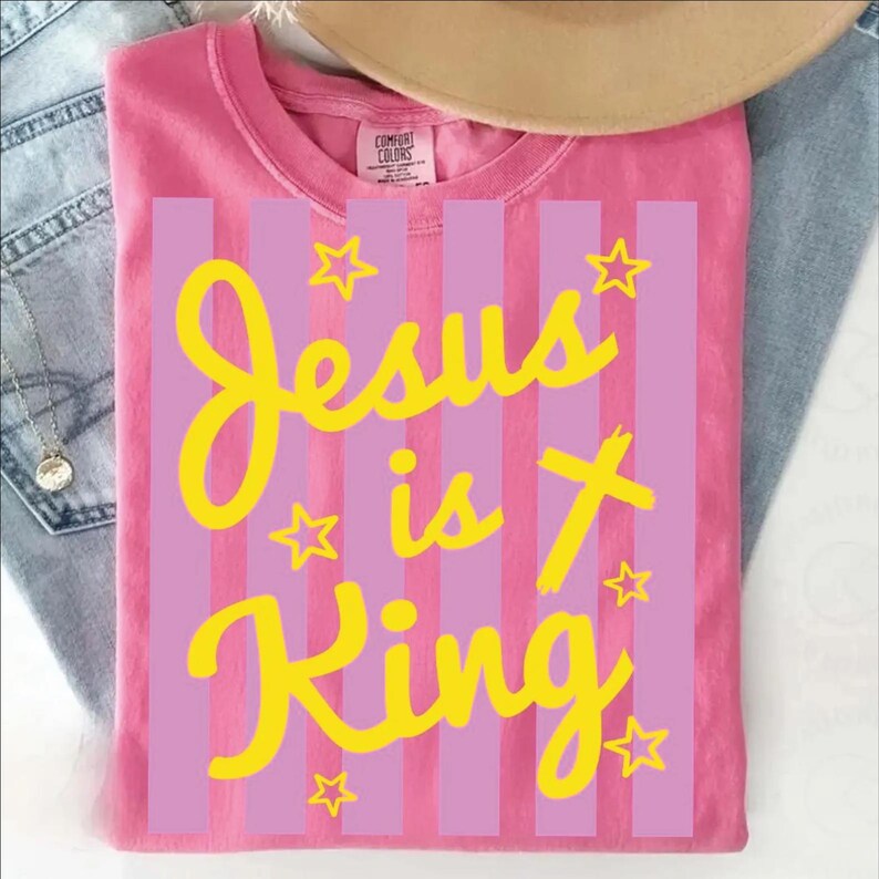 A pink t-shirt with yellow text and stars printed on it, along with a beige hat and some denim jeans.