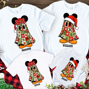 May include: White t-shirts and a onesie featuring a cartoon ghost character with Mickey Mouse ears, a Santa hat, and a patchwork quilt design in red, green, and white. Names are printed below the characters.