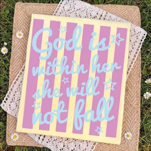 A colorful sign with the text "God is within her she will not fall" is displayed on a straw mat with white flowers.