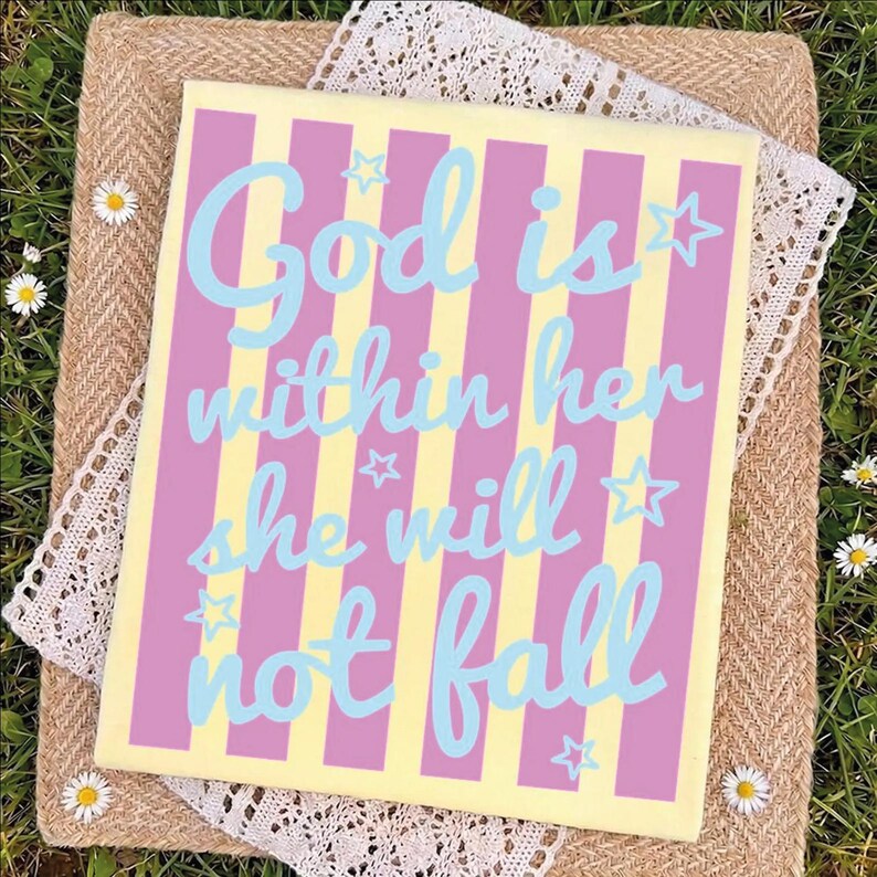 A colorful sign with the text "God is within her she will not fall" is displayed on a straw mat with white flowers.