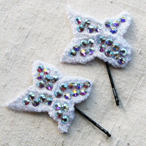May include: Two white butterfly hair clips with iridescent rhinestones. Each clip has a black bobby pin attached.