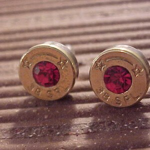 May include: A pair of gold-colored earrings made from .38 Special bullet casings with red gemstones set in the center.