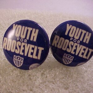 May include: Two blue and white political campaign buttons with the text "Youth for Roosevelt" and a small image of the American flag.