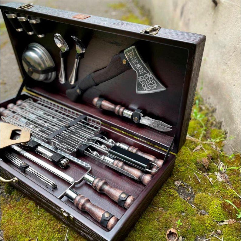 Puede incluir: Un juego de caja de madera con una variedad de herramientas para asar a la parrilla, incluyendo pinchos, una rejilla para asar, un peque&ntilde;o hacha y una esp&aacute;tula. La caja est&aacute; forrada con madera oscura y tiene un asa de cuero.