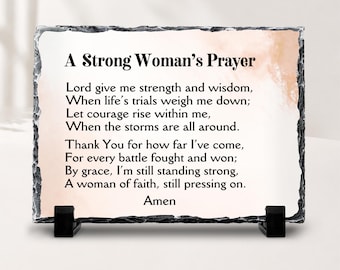 Puede incluir: Una placa de pizarra rectangular con bordes rugosos y cincelados que presenta el texto impreso A Strong Woman's Prayer, seguido de un verso sobre fuerza, sabiduría y fe. La placa se apoya sobre dos pequeños soportes de plástico negro.