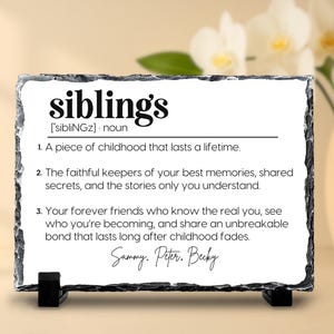 May include: A rectangular slate plaque with the definition of "siblings" printed in black. The definition includes three points about siblings and is supported by a black stand. The names Sammy, Peter, and Becky are signed at the bottom.