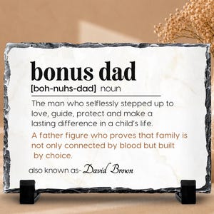 May include: A rectangular slate plaque with rough, dark gray edges and a white center. The text reads: bonus dad [boh-nuhs-dad] noun. The man who selflessly stepped up to love, guide, protect and make a lasting difference in a child's life.