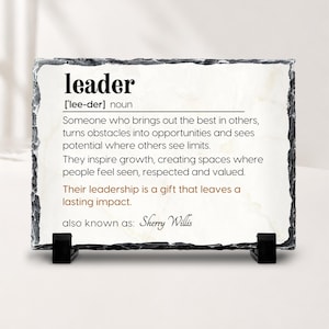 May include: A rectangular slate plaque with rough, dark gray edges and a smooth white center. The text defines the word leader, followed by the phrase also known as: Sherry Willis. The plaque is supported by two small black plastic stands.