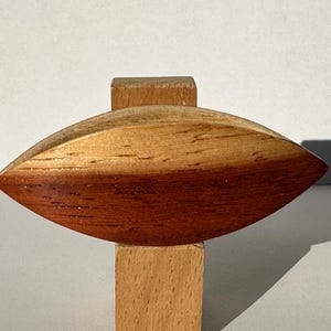 May include: A wooden sculpture of a boat with a rounded hull, made of two different shades of wood. The boat is sitting on a wooden base.