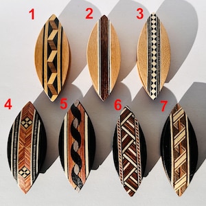 Op de afbeelding: Een verzameling van zeven houten decoratieve items in de vorm van een surfboard. Elk stuk heeft unieke geometrische patronen en ontwerpen in verschillende tinten bruin, zwart en natuurlijke houttinten. De items zijn gerangschikt op een lichtgekleurd oppervlak.
