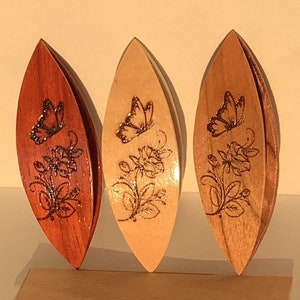 Puede incluir: Tres devanadores de hilo de madera con un diseño de mariposa y flores. Los devanadores son en tonos de marrón y madera natural.