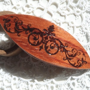 May include: A wooden thread holder with a decorative floral design burned into the surface. The holder is a reddish brown color and the design is black.