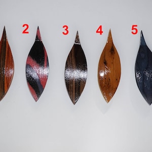 Op de afbeelding: Vijf houten bladvormige ornamenten met verschillende houtnerfpatronen en kleuren. De ornamenten zijn genummerd van 1 tot en met 5.