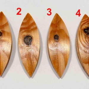 Op de afbeelding: Vier houten blad-vormige hangers met natuurlijke houtnerf en knopen. Elke hanger is lichtbruin van kleur met een donkerdere knoop in het midden. De hangers zijn in een rij gerangschikt en tonen hun unieke houtpatronen.