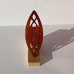 May include: A wooden Celtic knot design in the shape of a heart, carved from a reddish-brown wood. The design is mounted on a small wooden stand.