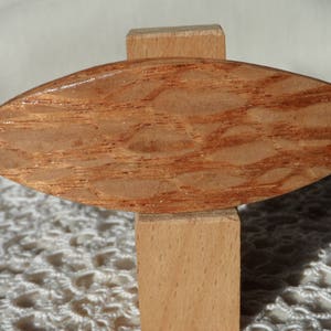Op de afbeelding: Een houten decoratief object in de vorm van een blad, met een natuurlijk houtnerfpatroon. Het is gemonteerd op een kleine, rechthoekige houten basis. Het hout heeft een warme, roodbruine tint.