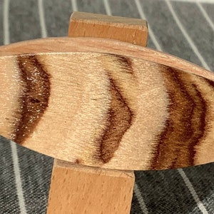 May include: A wooden oval-shaped object with a brown and white striped pattern. The object is mounted on a wooden stand.