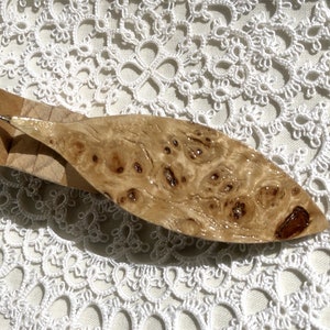 Op de afbeelding: Een houten haaknaald met een bruin en beige burlhouten handvat. De haaknaald is bevestigd aan een houten basis.