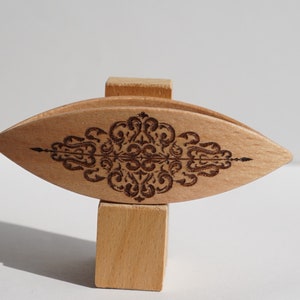 Op de afbeelding: Een houten garenkom met een decoratief ontwerp dat in het oppervlak is gegraveerd. De kom is oogvormig en staat op een houten standaard.