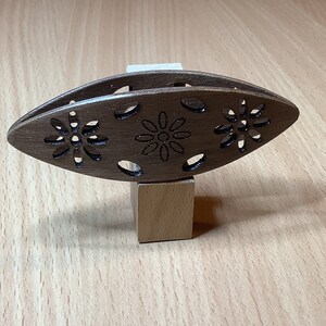 以下が含まれることがあります： 花柄が彫刻された木製糸巻きボウル。ボウルは茶色で、滑らかな仕上がりです。木製のブロックの上に置かれています。