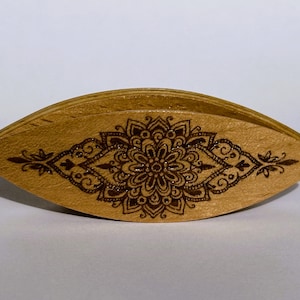 May include: A wooden yarn bowl with a brown mandala design. The bowl is shaped like a teardrop and has a smooth, polished finish.