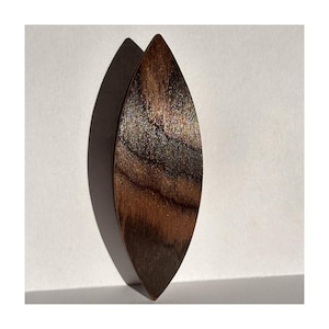 May include: A wooden, leaf-shaped object with a dark brown, natural wood grain pattern. The object is elongated and tapered, with a smooth, polished surface. The wood grain features lighter brown streaks and variations in color. The object casts a shadow on a white background.