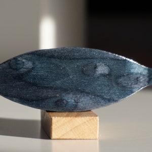 May include: A dark blue wooden leaf-shaped sculpture with a silver metallic finish. The sculpture is displayed on a small wooden base.