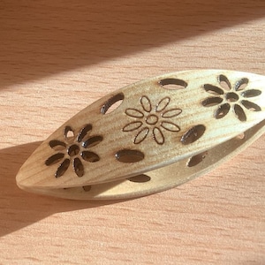 Op de afbeelding: Een houten garenkom met een gesneden bloemenpatroon. De kom is lichtbruin en heeft een gladde afwerking.