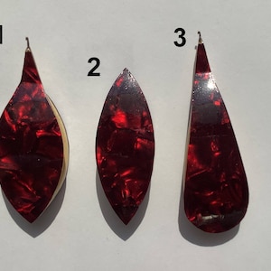 May include: Three red guitar picks with a marbled pattern. The picks are numbered 1, 2, and 3.