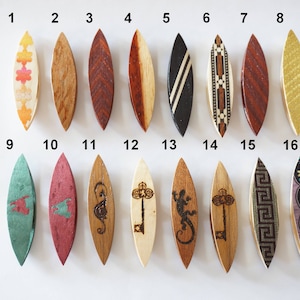 Könnte beinhalten: Sechzehn hölzerne Garnrollen-Maschenmarkierer mit verschiedenen Designs, darunter geometrische Muster, Tiere und Schlüssel. Die Markierer sind von 1 bis 16 nummeriert.