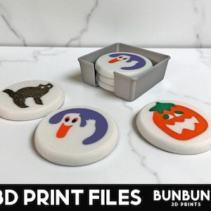 May include: A set of Halloween-themed coasters with a gray holder. The coasters feature a black cat, a ghost, and a jack-o'-lantern design. The text "3D PRINT FILES" is at the bottom of the image.