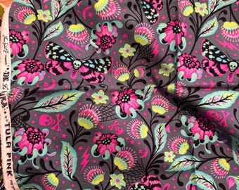 May include: A dark gray fabric featuring a repeating pattern of moths with skull markings, pink and yellow flowers, black swirling vines, small stars, crescent moons, and pink lightning bolts. The white selvage edge displays the text Free Spirit Presents De La Luna by Tula Pink.