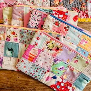 Puede incluir: Una colección de estuches rectangulares con cremallera hechos de parches de tela acolchada. Cada estuche presenta un diseño de patchwork con varios estampados florales, frutales y de patrones en colores pastel y vivos.