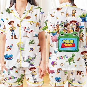 May include: A white short-sleeve button-down pajama shirt and matching shorts set featuring a colorful Toy Story character print, yellow piping, and a green frame graphic on the back with the text YOUR TEXT and YOU'VE GOT A FRIEND IN ME.