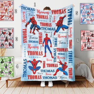 May include: A personalized blue and white blanket featuring the name "Thomas" in red and white, along with illustrations of Spider-Man in various poses. The blanket is a soft, cozy item, perfect for a bedroom or living room.
