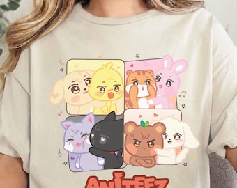 Könnte beinhalten: Beiges T-Shirt mit einem farbenfrohen Aufdruck von Cartoon-Tieren in quadratischen Rahmen, darunter ein Hund, ein Küken, eine Katze, ein Bär und ein Kaninchen. Das Wort "AniteeZ" ist in roten Blockbuchstaben darunter gedruckt. Das Shirt ist aus weichem Material.