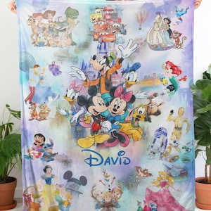 Op de afbeelding: Een kleurrijke deken met verschillende Disney-personages, waaronder Mickey en Minnie Mouse, Goofy, Donald Duck en personages uit Star Wars en Disney Princess-films. De naam "DAVID" is in blauwe letters geschreven.