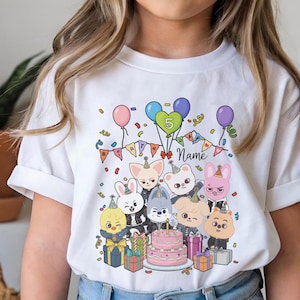 May include: White t-shirt featuring a colorful birthday design. The graphic includes cartoon animal characters, balloons, confetti, a cake, and the number 5. The word "Name" is also visible.