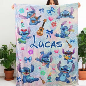 Op de afbeelding: Een gepersonaliseerde deken met het personage Stitch uit Lilo & Stitch. De deken heeft een pastelkleurige achtergrond met Stitch-illustraties, ukeleles, strikken en de naam "Lucas" in blauw schrift. Het ontwerp bevat harten en tropische bloemen.