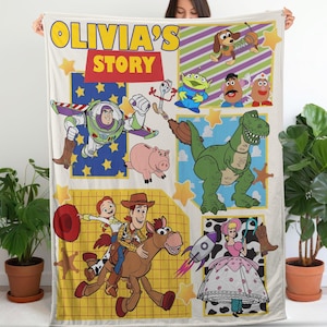 Op de afbeelding: Een cr&egrave;mekleurige deken met een patchwork-ontwerp met Toy Story-personages. De deken bevat Buzz Lightyear, Woody, Jessie, Rex en anderen, met de tekst "OLIVIA'S STORY" in geel en rood.