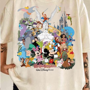 Puede incluir: Camiseta color crema con un gr&aacute;fico colorido de varios personajes de Disney, incluyendo Mickey y Minnie Mouse, Dumbo y Peter Pan. Las palabras "Magic Kingdom" y "Walt Disney World" est&aacute;n impresas debajo.