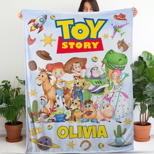 Puede incluir: Una manta de forro polar azul claro con el logotipo de Toy Story, el nombre Olivia y varios personajes como Woody, Jessie, Buzz Lightyear, Rex y el Sr. Patata, rodeados de coloridas ilustraciones de cohetes, estrellas y sombreros.