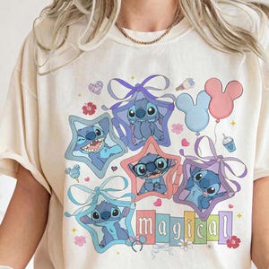 Może przedstawiać: Kremowa koszulka z kolorową grafiką postaci Stitch w ramkach w kształcie gwiazd z kokardkami, balonami i napisem "magical". Projekt zawiera r&oacute;żne wyrazy twarzy Stitch i pastelowe kolory.