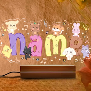 May include: A personalized night light with the word "name" in colorful letters, adorned with cartoon animals and musical notes. The light sits on a wooden base and is connected to a power cord.